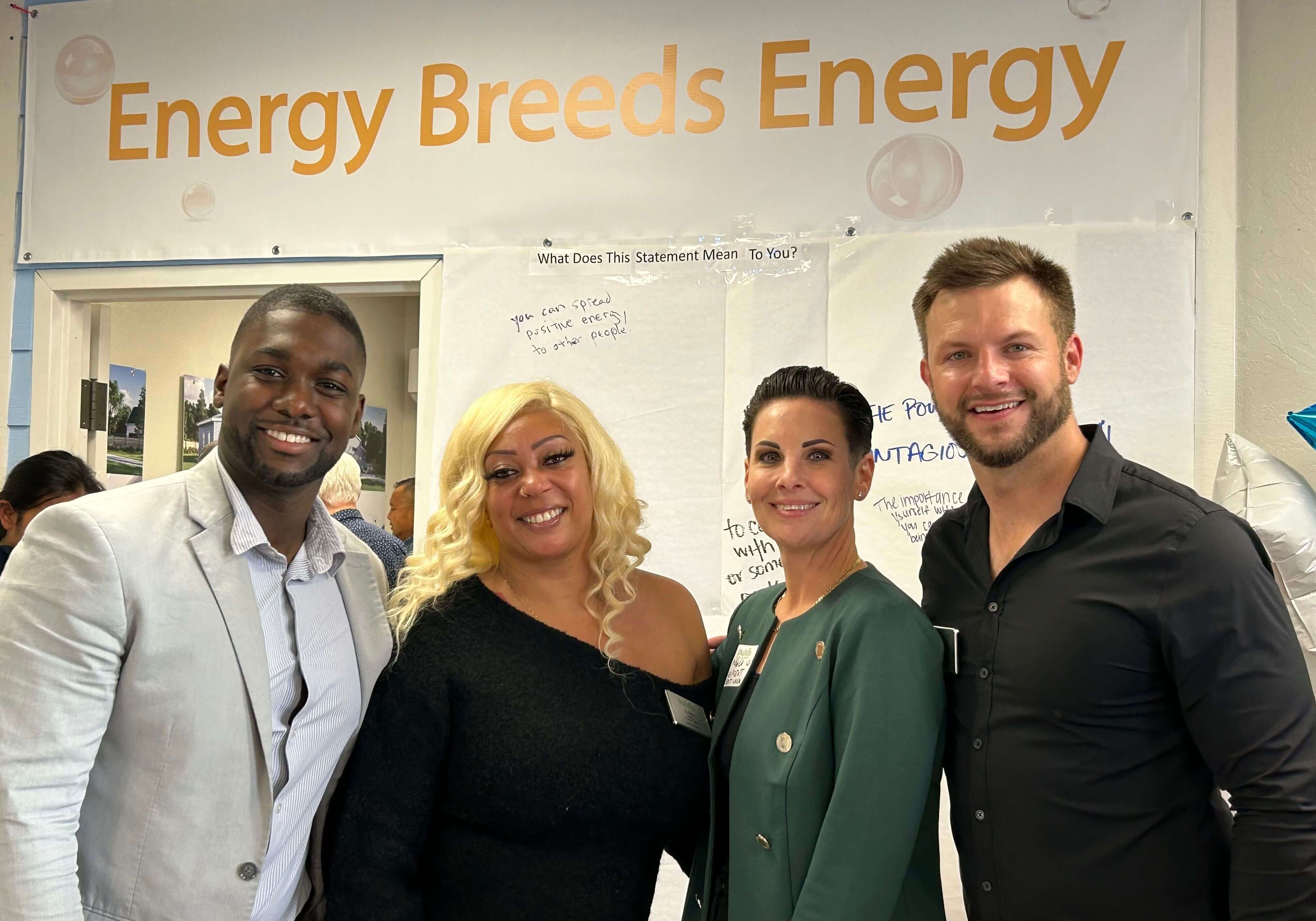 four people smiling in front of a sign reading "energy buids energy"